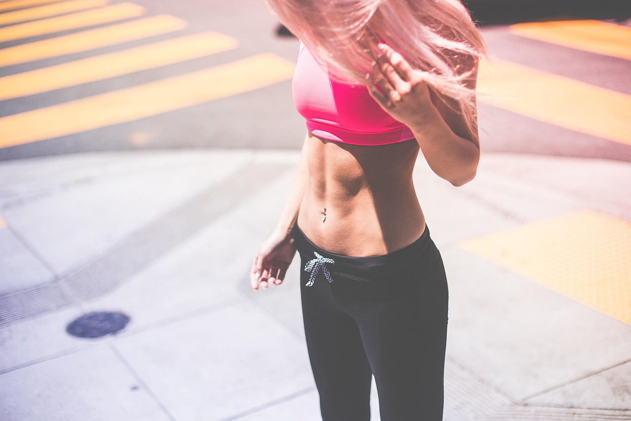 A young woman standing on a sidewalk with her back to the camera. She is wearing a pink sports bra and black leggings with a ...