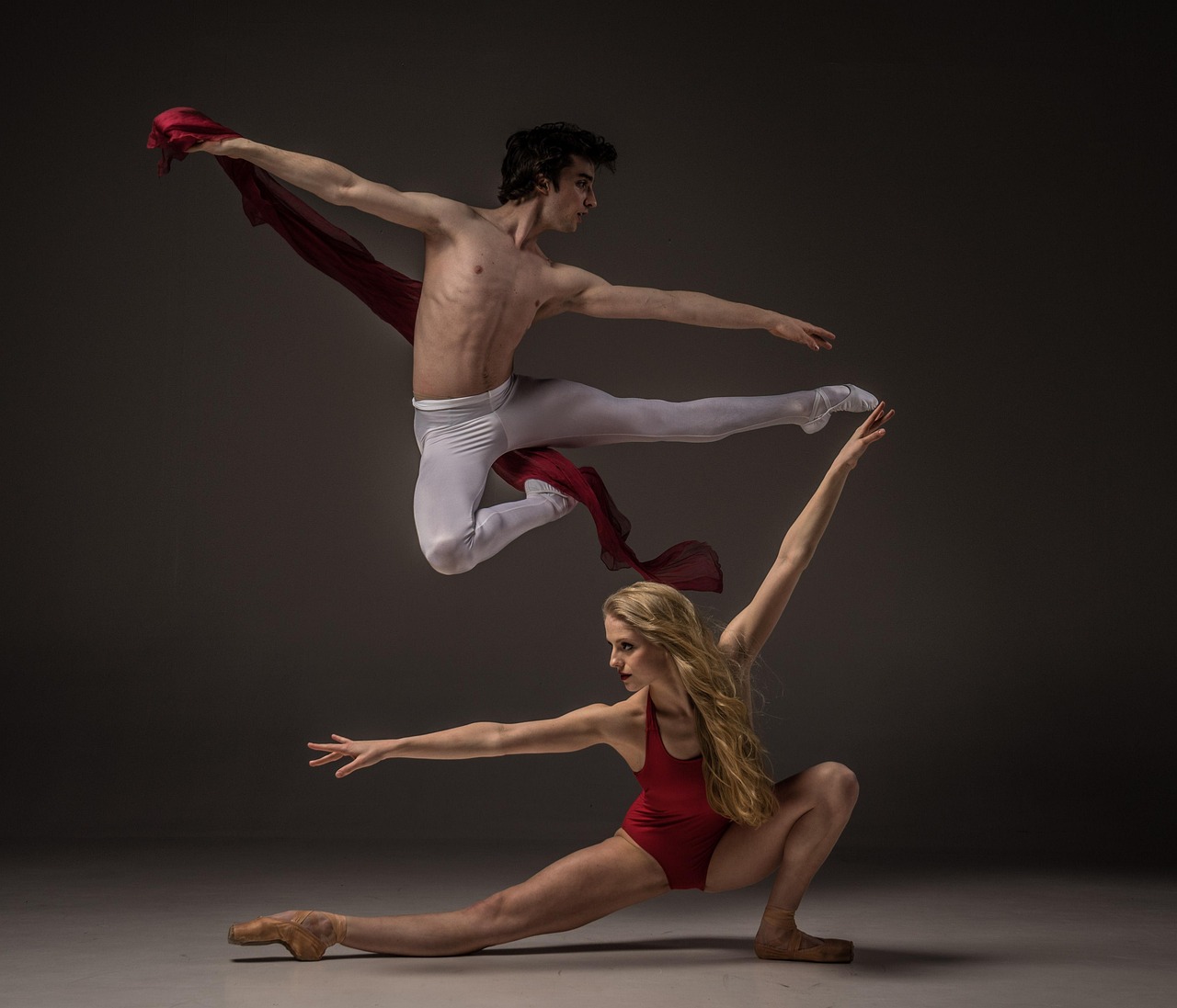 A ballet dancer and a ballerina in a studio setting. The dancer is in the air, with his arms stretched out to the sides and h...