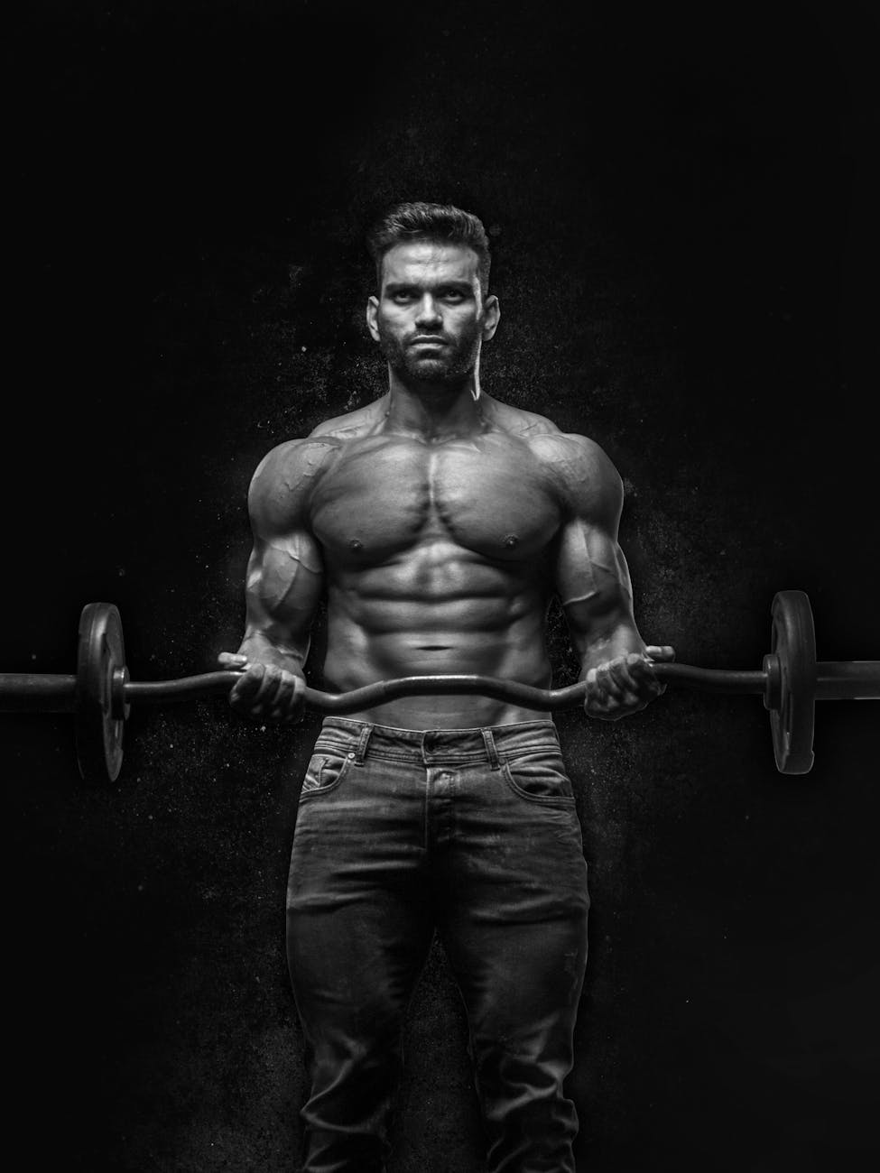 A black and white portrait of a muscular man lifting a barbell. He is standing in front of a dark background and is holding t...