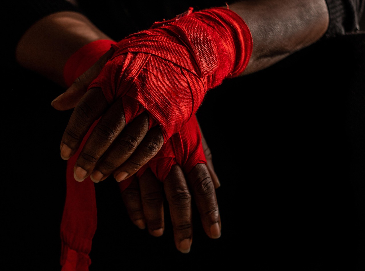 A pair of hands wrapped in red bandages. The hands appear to be of African descent and are resting on a black surface. The ba...