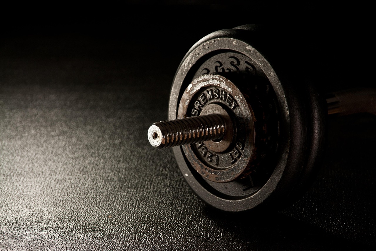 A close-up of a dumbbell. The dumbbell is black in color and has a round base with a textured surface. The text on the base r...