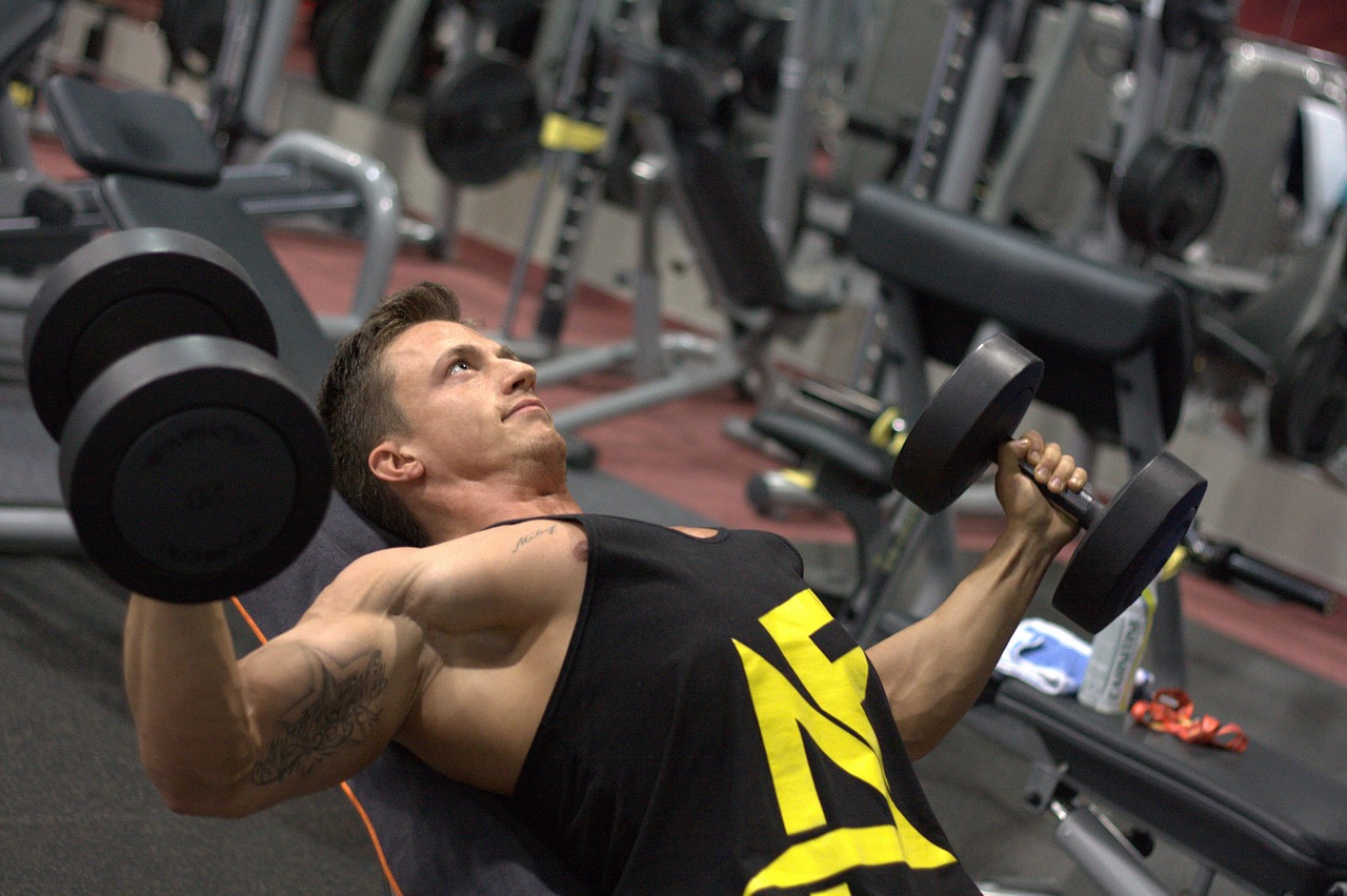 A young man lifting weights in a gym. He is lying on a bench with his feet shoulder-width apart and his arms extended above h...