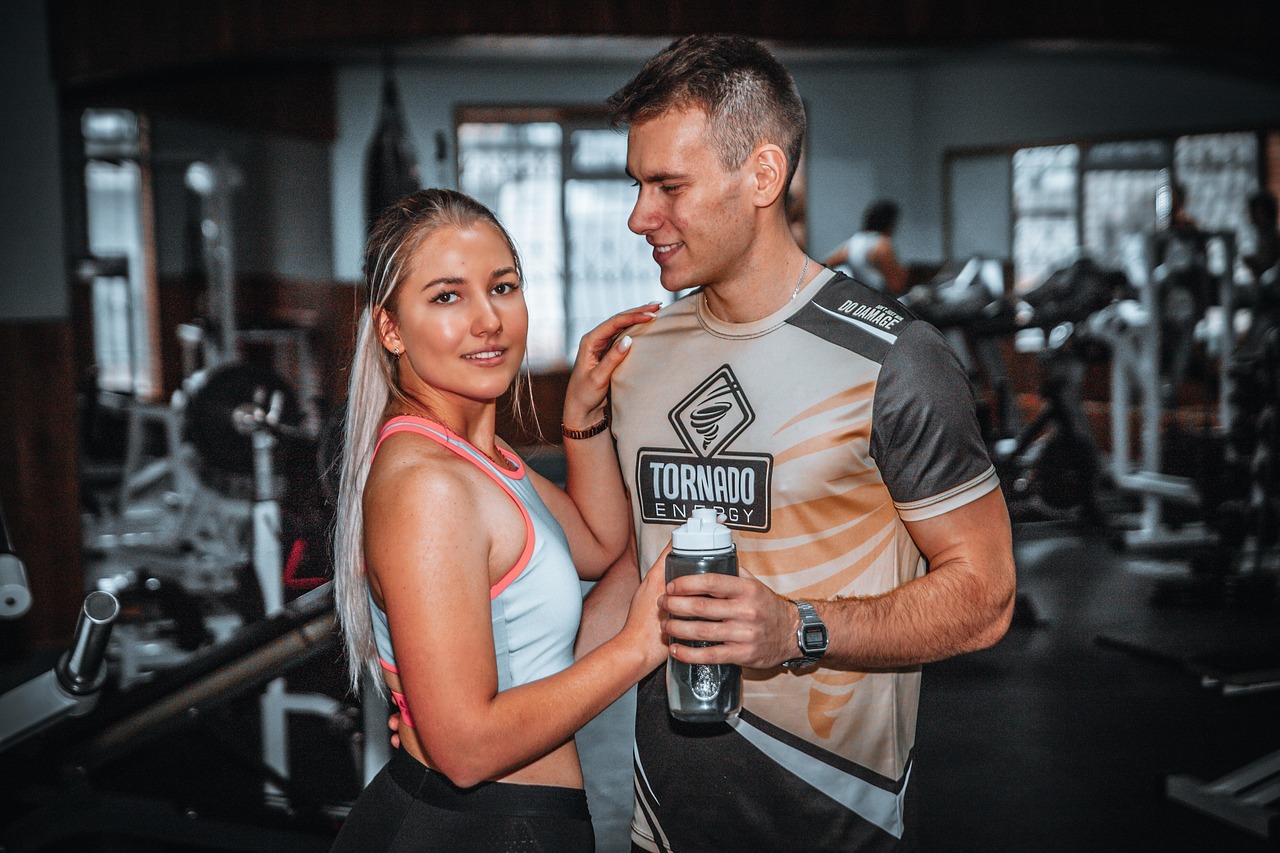 A young man and woman in a gym. The man is wearing a black and orange t-shirt with the word "Tornado" written on it and a wat...