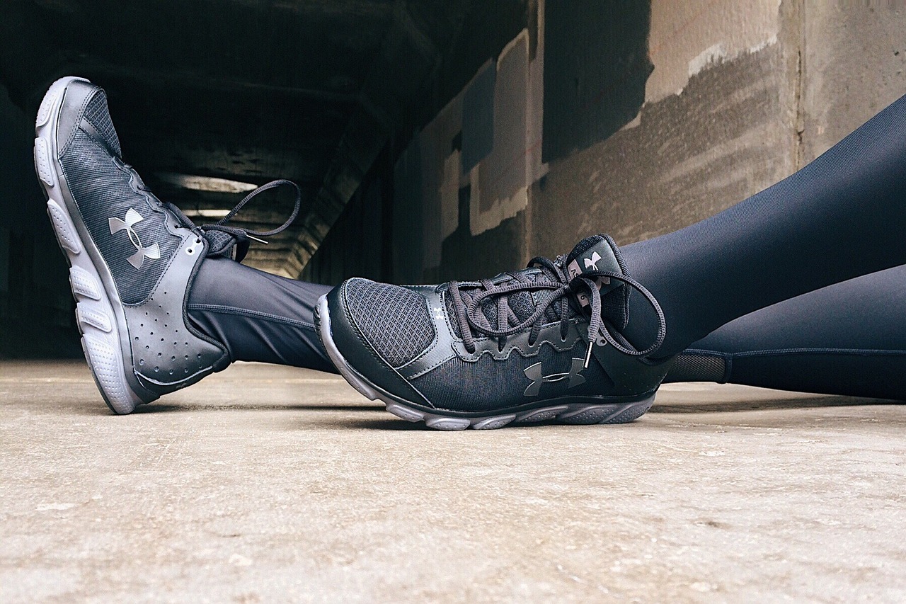 A pair of feet resting on a concrete floor. The person is wearing black leggings and black Under Armour sneakers. The sneaker...