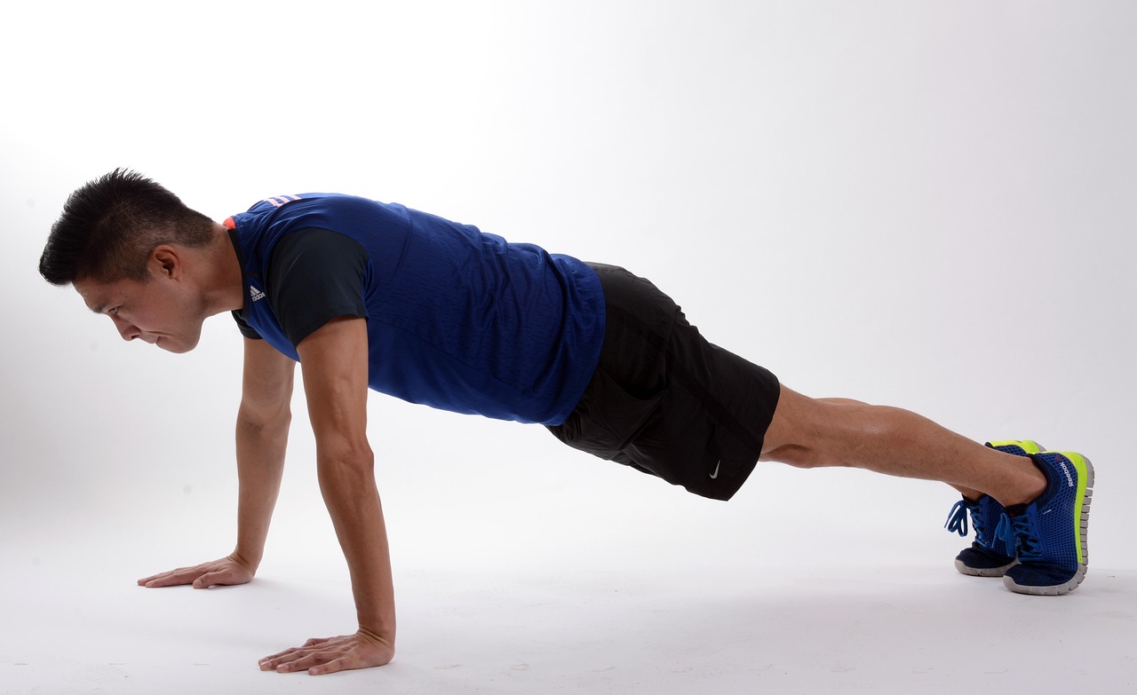 A young man performing a plank exercise. He is wearing a blue t-shirt and black shorts, and blue and yellow running shoes. Hi...