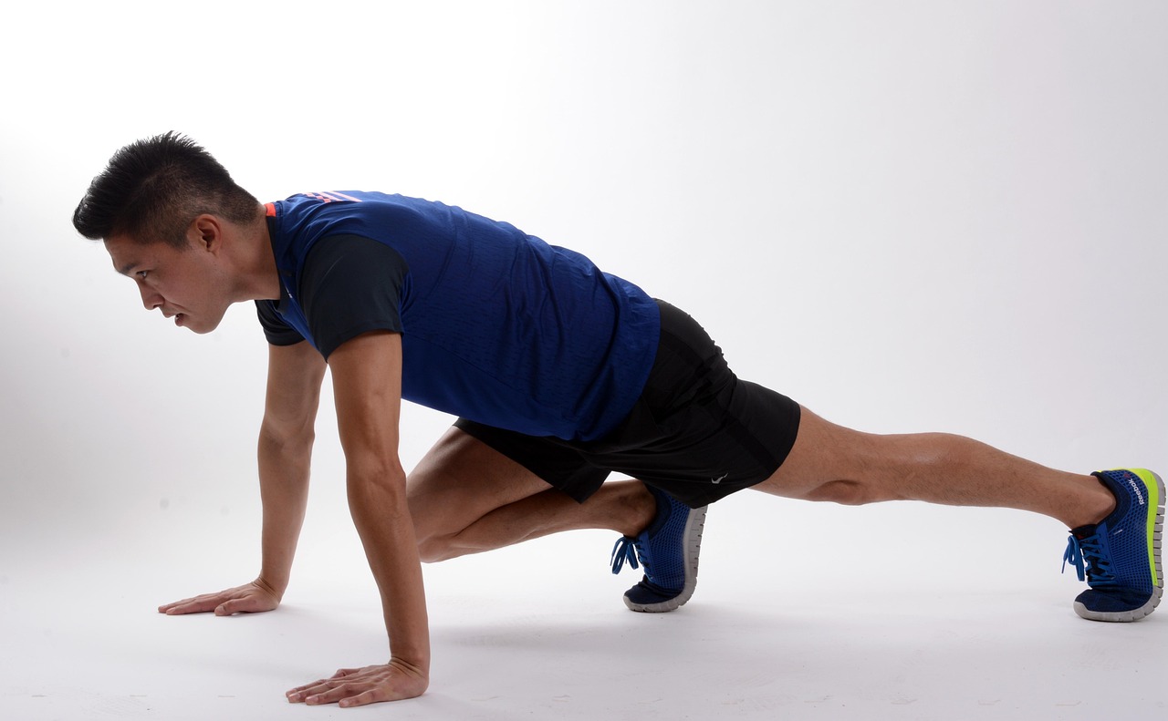 A young man in a blue t-shirt and black shorts performing a plank exercise. He is in a crouched position with his hands on th...