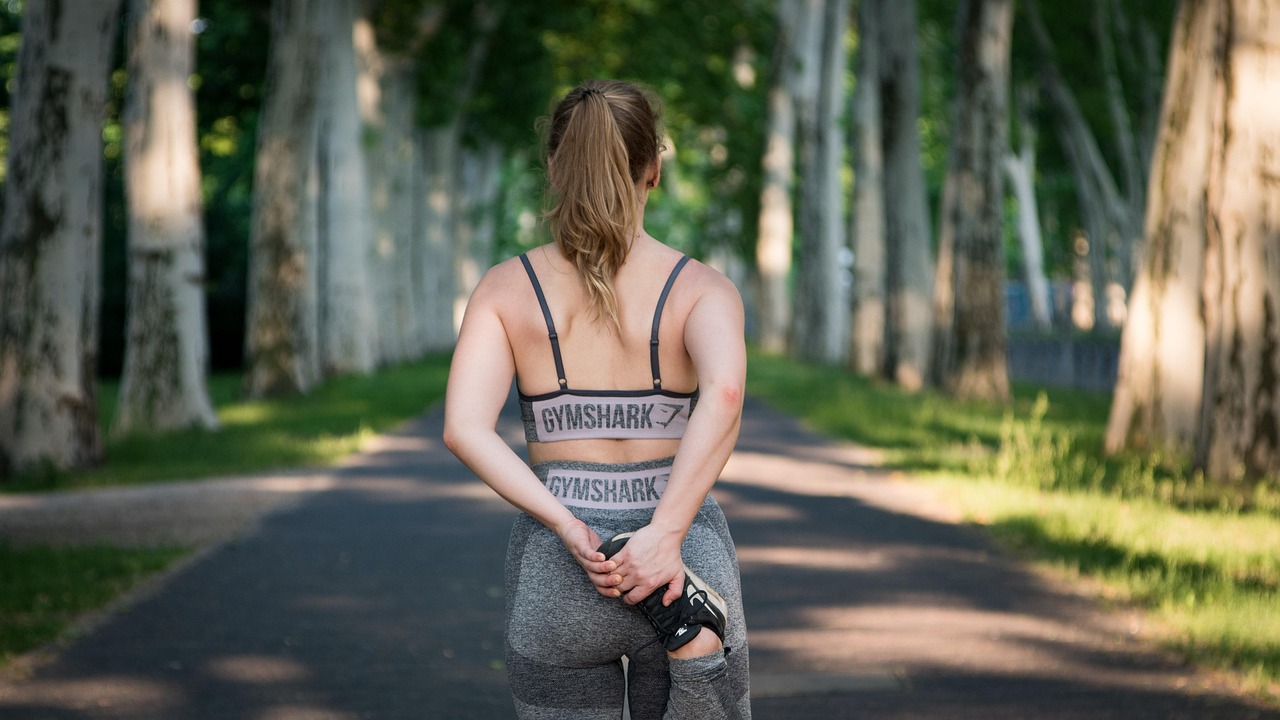 A young woman standing on a pathway in a park. She is wearing a black sports bra with the word "Gymnastics" written on it and...