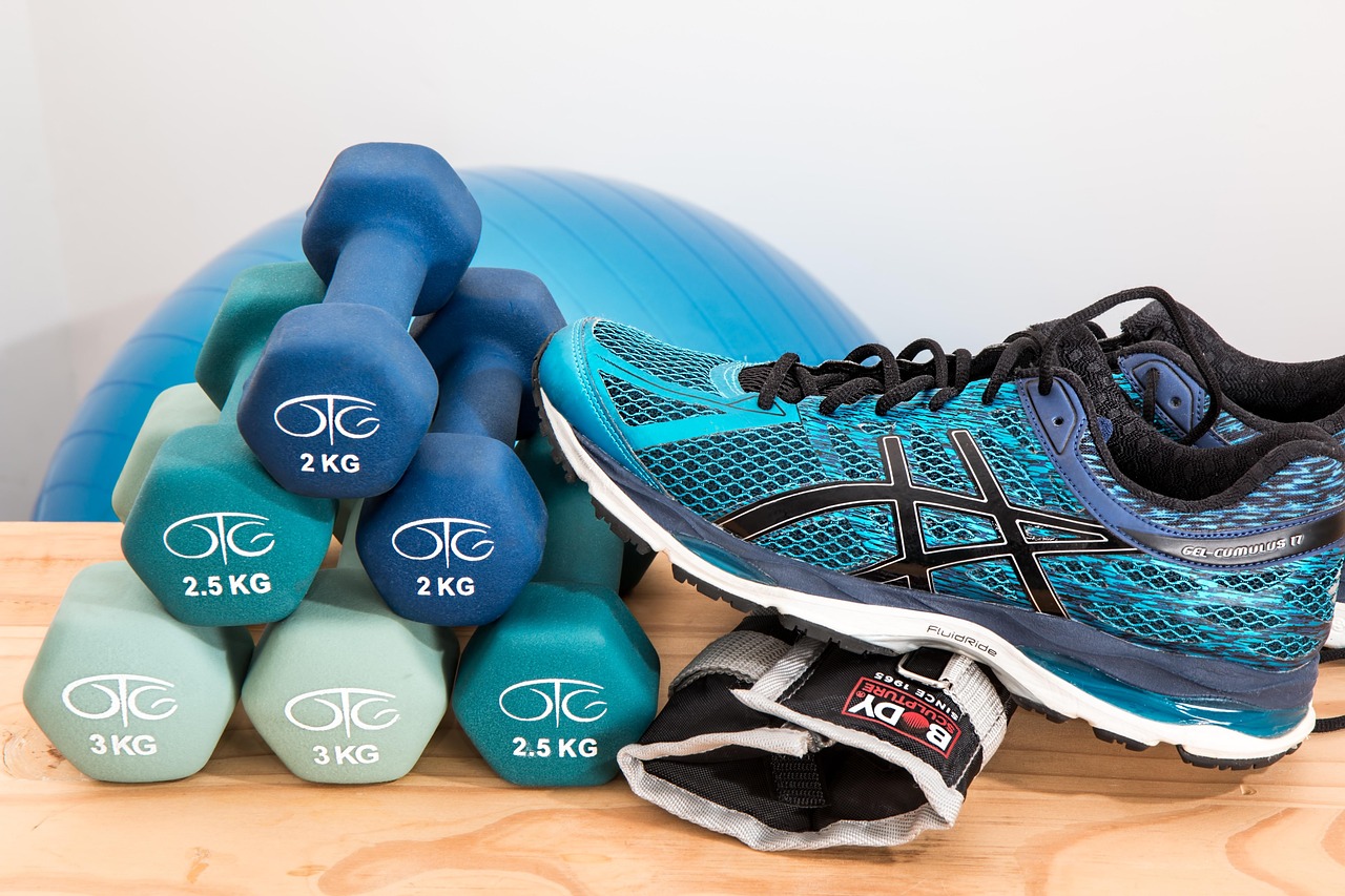 A pair of blue and black Asics running shoes and a set of dumbbells on a wooden surface. The dumbbell on the left side of the...