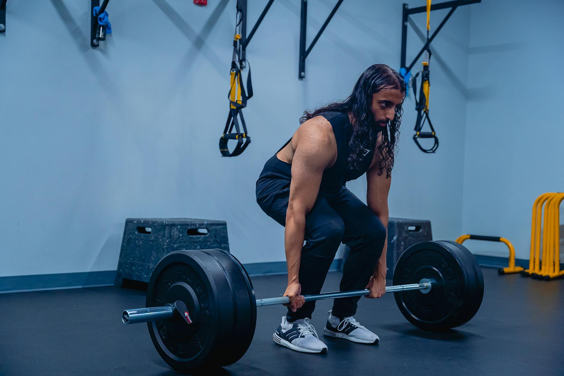 A young man lifting a barbell in a gym. He is in a squat position with his feet shoulder-width apart and his arms extended ab...