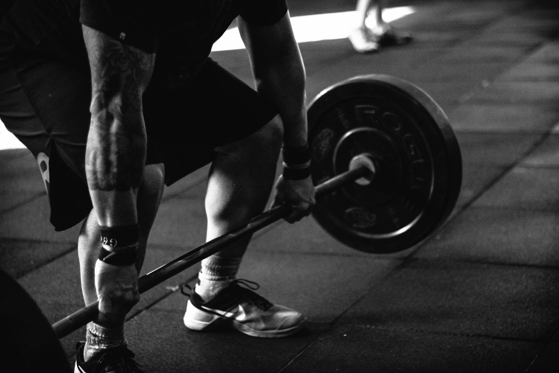 A black and white photograph of a person lifting a barbell. The person is in the middle of a weightlifting exercise, with the...