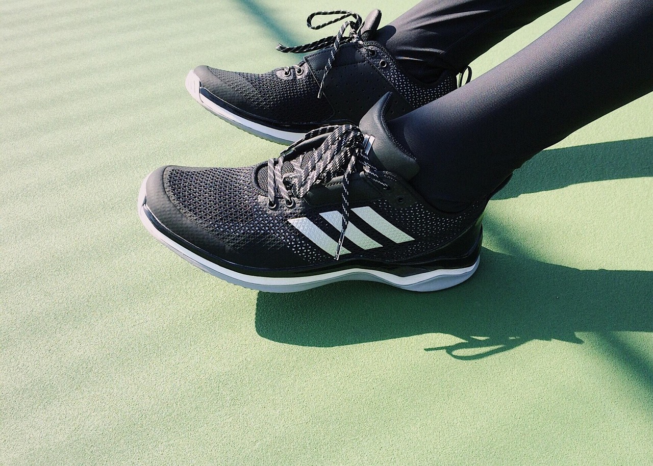 A pair of black Adidas running shoes on a green surface. The shoes have a white sole and black laces. The Adidas logo is visi...
