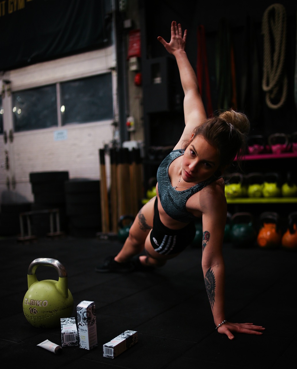 A young woman in a gym, performing a push-up exercise. She is wearing a black sports bra and black shorts, and her hair is pu...