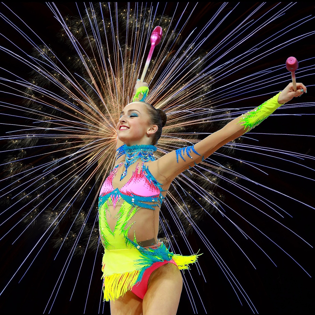 A young woman performing a rhythmic gymnastics routine. She is wearing a colorful outfit with a pink and green color scheme a...