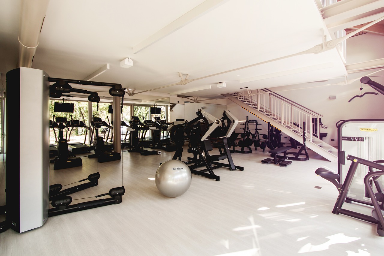 A modern and spacious gym with a high ceiling and white walls. The floor is made of light-colored wood and the walls are pain...