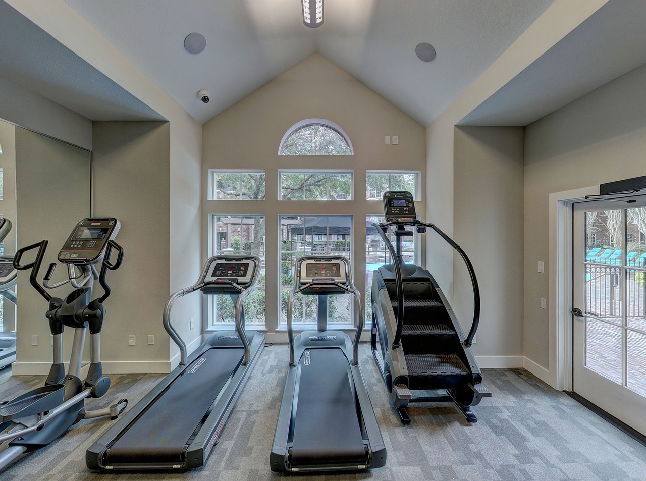 A modern and well-equipped gym with three treadmills and elliptical machines. The room has a high ceiling with recessed light...