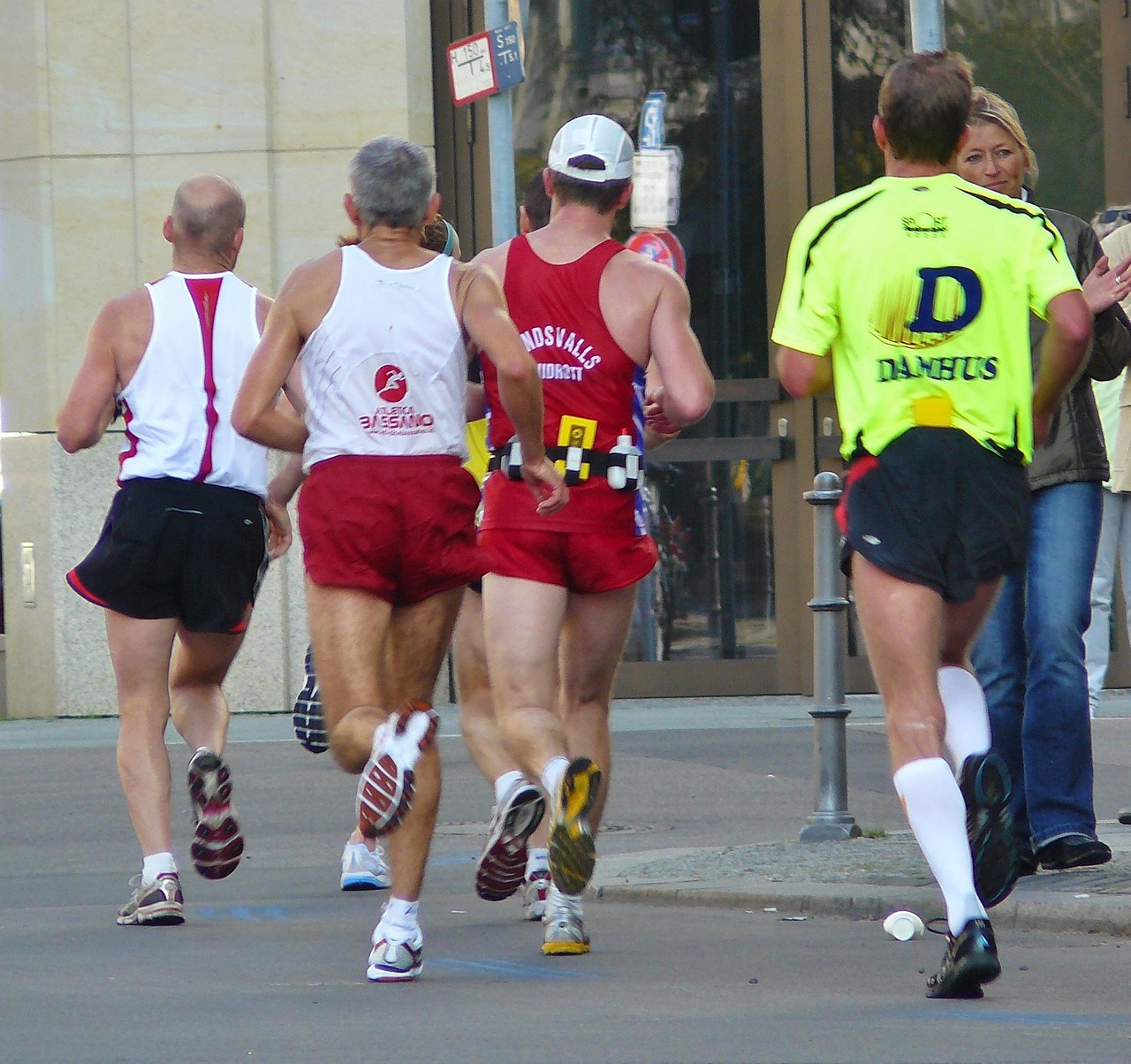 A group of four men running on a street. They are all wearing red and white running gear and appear to be in the middle of a ...