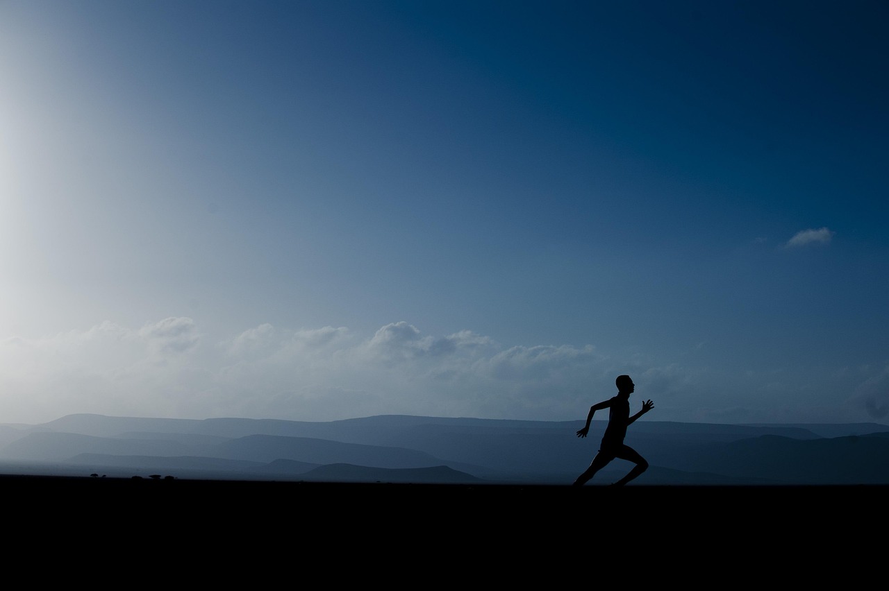 A silhouette of a person running on a vast landscape. The person is in mid-stride, with their arms and legs stretched out in ...