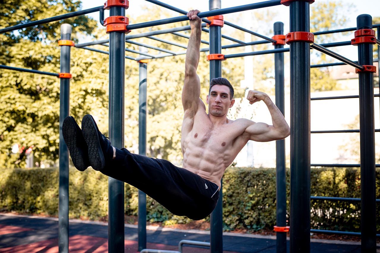 A young man performing a pull-up exercise on a horizontal bar in a park. He is shirtless and is wearing black shorts and blac...
