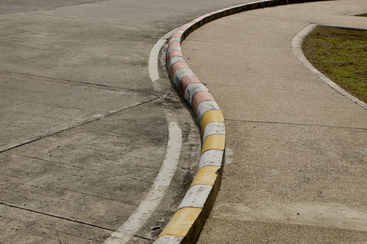 A curved road with a yellow and white striped barrier on one side. The barrier is made up of three sections, with the top sec...