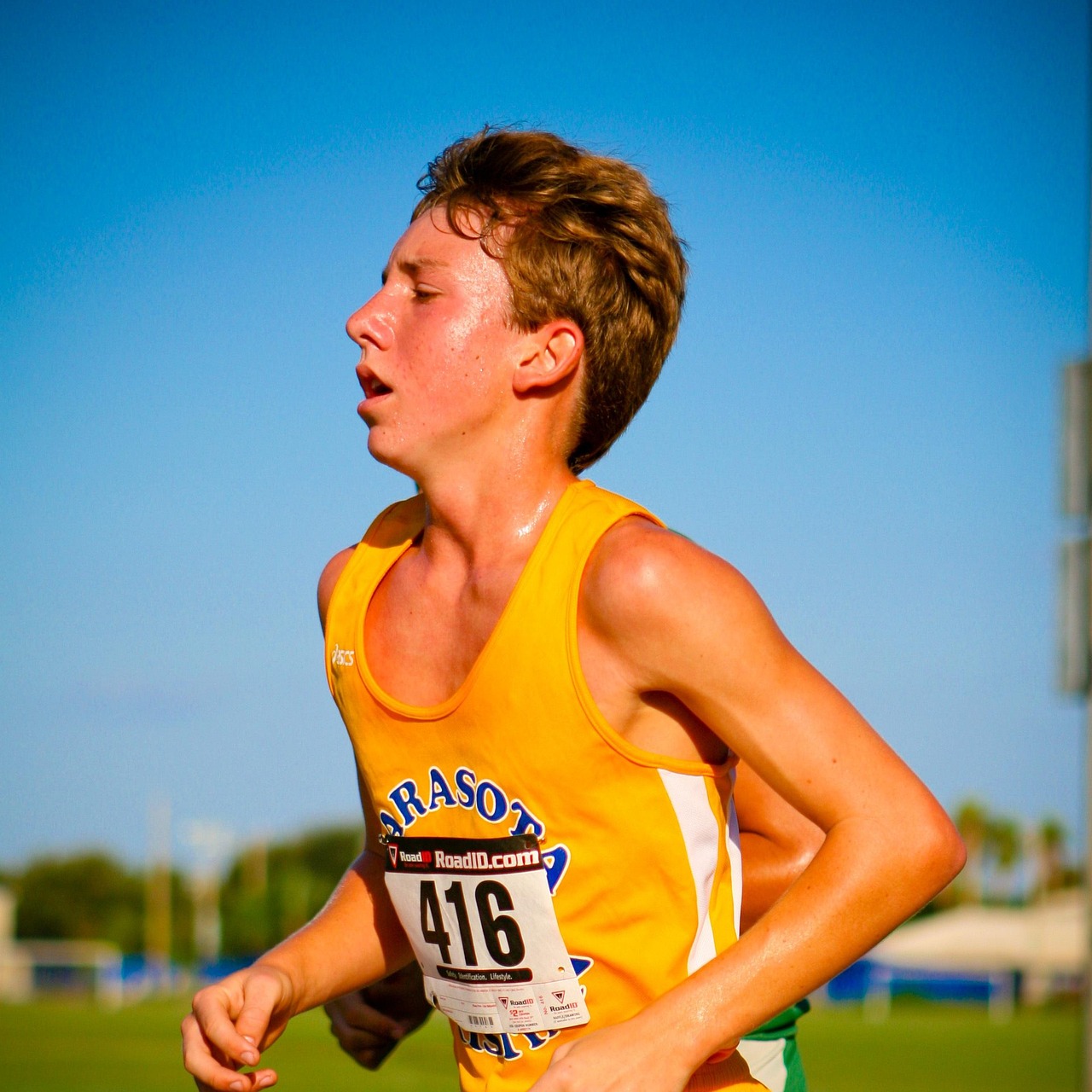A young male athlete running on a track. He is wearing a yellow tank top with the number 416 on it and green shorts. He has s...