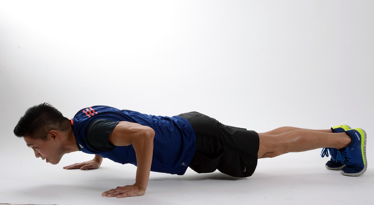 A young man performing a plank exercise. He is wearing a blue t-shirt, black shorts, and blue and yellow running shoes. His a...