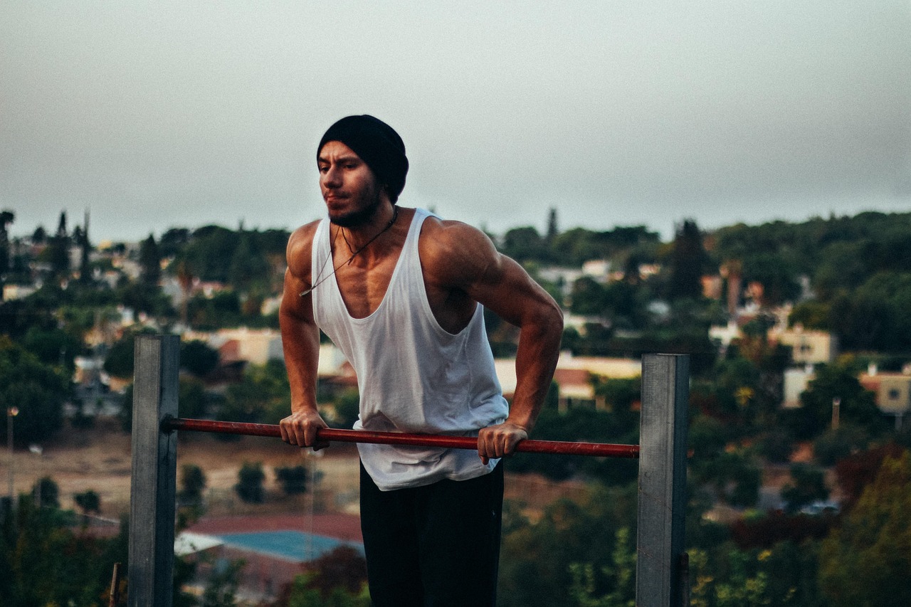 A young man standing on top of a metal structure with his hands on the bars. He is wearing a white tank top and black pants. ...