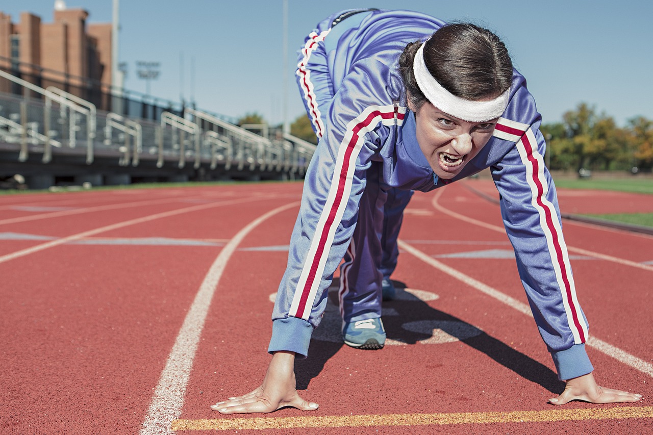 A young woman on a running track. She is wearing a blue tracksuit with red and white stripes on the sleeves and a white headb...