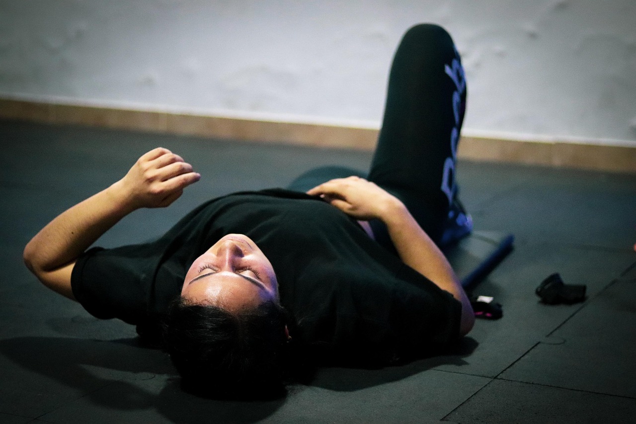 A young man lying on his back on the floor with his arms stretched out to the sides. He is wearing a black t-shirt and black ...