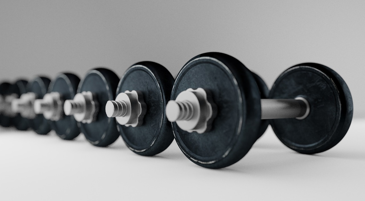 A row of dumbbells lined up in a row on a white background. The dumbbell weights are black in color and appear to be made of ...
