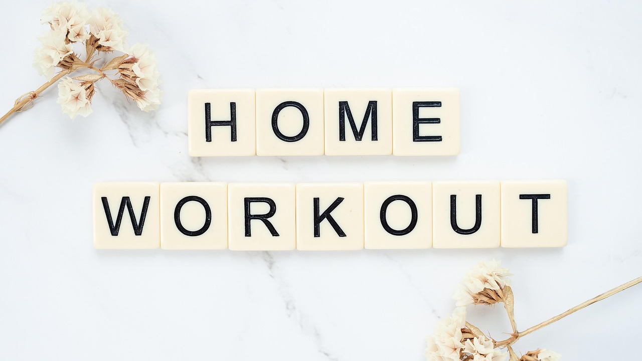 A flat lay of the words "HOME WORKOUT" spelled out using Scrabble tiles. The tiles are arranged in a horizontal line on a whi...