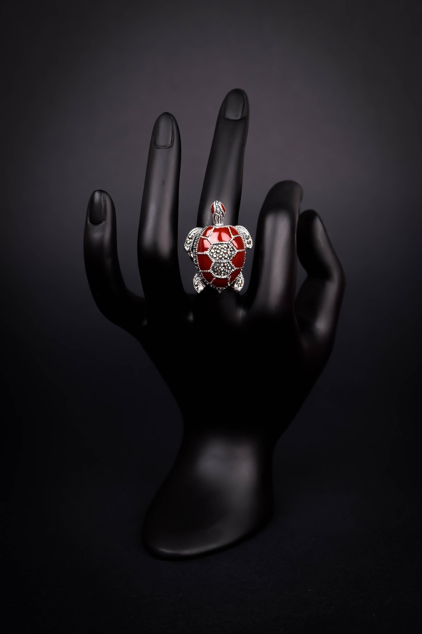 A black hand with a ring on it. The hand is positioned in a way that the fingers are slightly spread apart. The ring is made ...