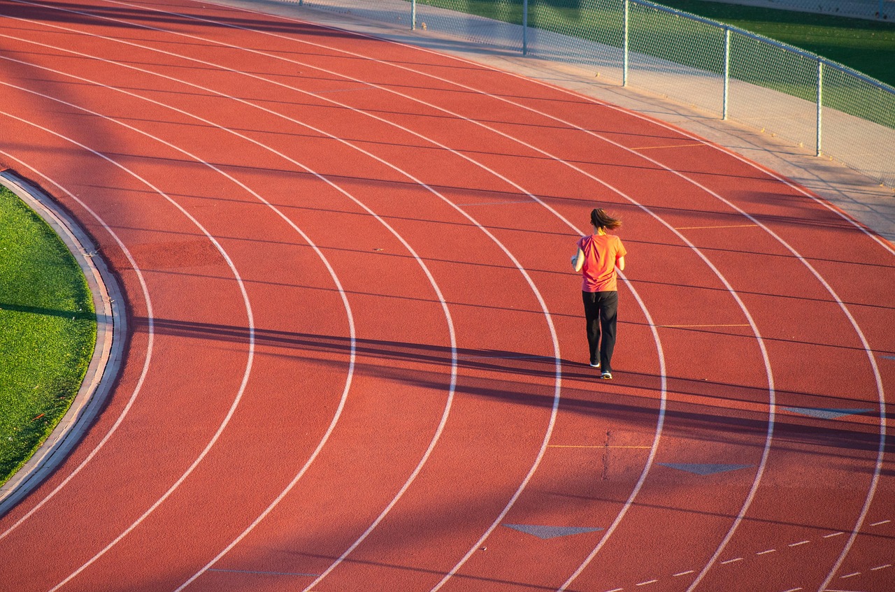 A person walking on a running track. The track is red in color and has white lines marking the lanes. The person is wearing a...