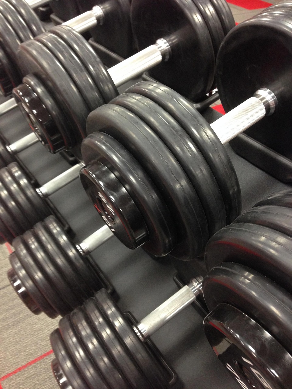 A row of dumbbells in a gym. There are six pairs of weights in total, arranged in a neat and orderly manner. The weights are ...