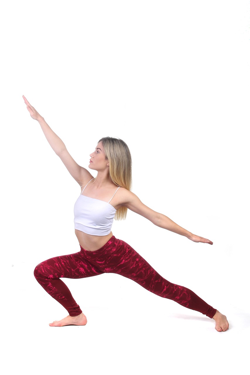 A young woman in a yoga pose. She is wearing a white crop top and maroon leggings with a floral pattern. Her arms are stretch...