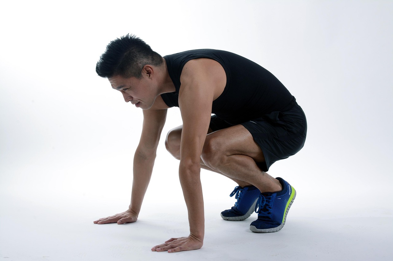 A young man in a black tank top and shorts, crouching down with his hands on the ground. He appears to be in the middle of a ...