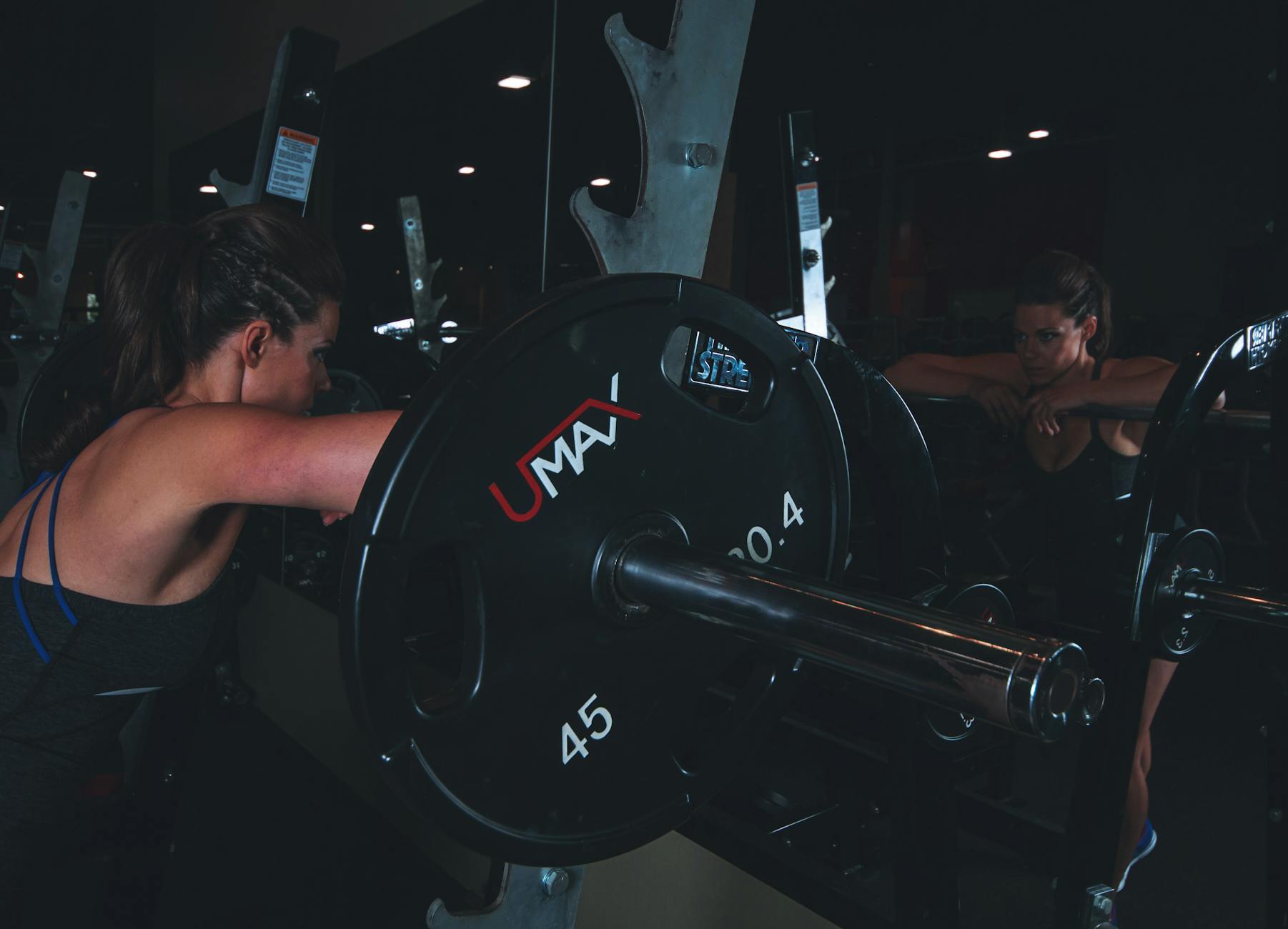 Two young women working out in a gym. They are both wearing workout clothes and are using a barbell with weights attached to ...