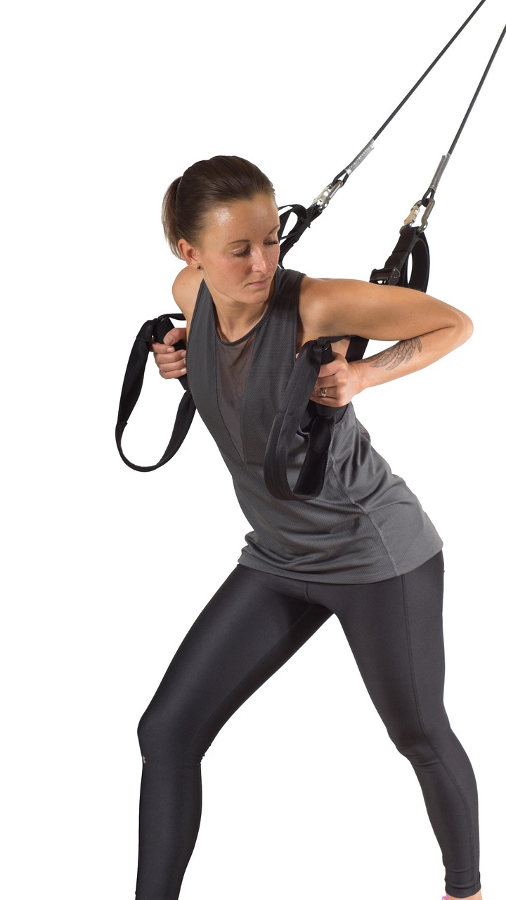 A young woman performing an exercise with a TRX suspension trainer. She is wearing a gray tank top and black leggings, and he...