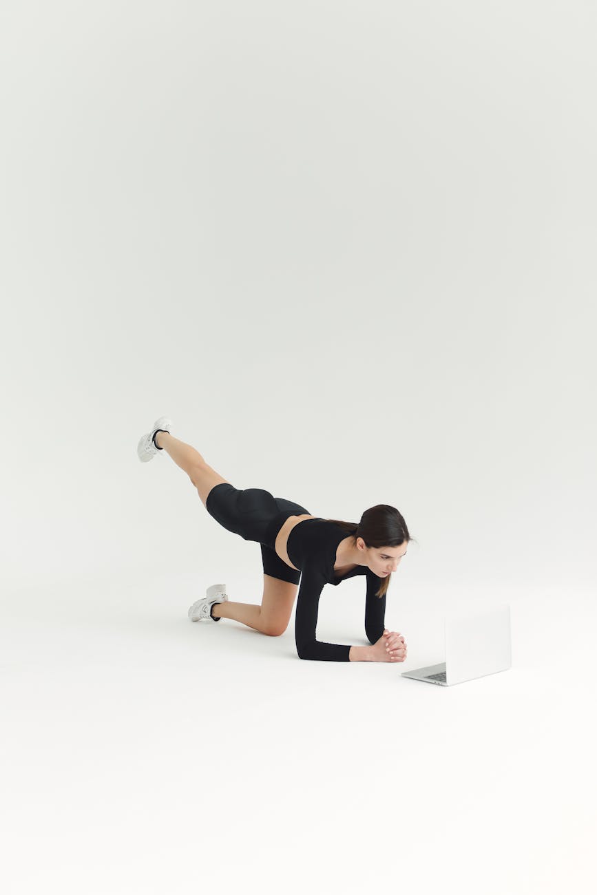 A young woman performing a plank exercise on a white background. She is wearing a black sports bra and black leggings, and wh...