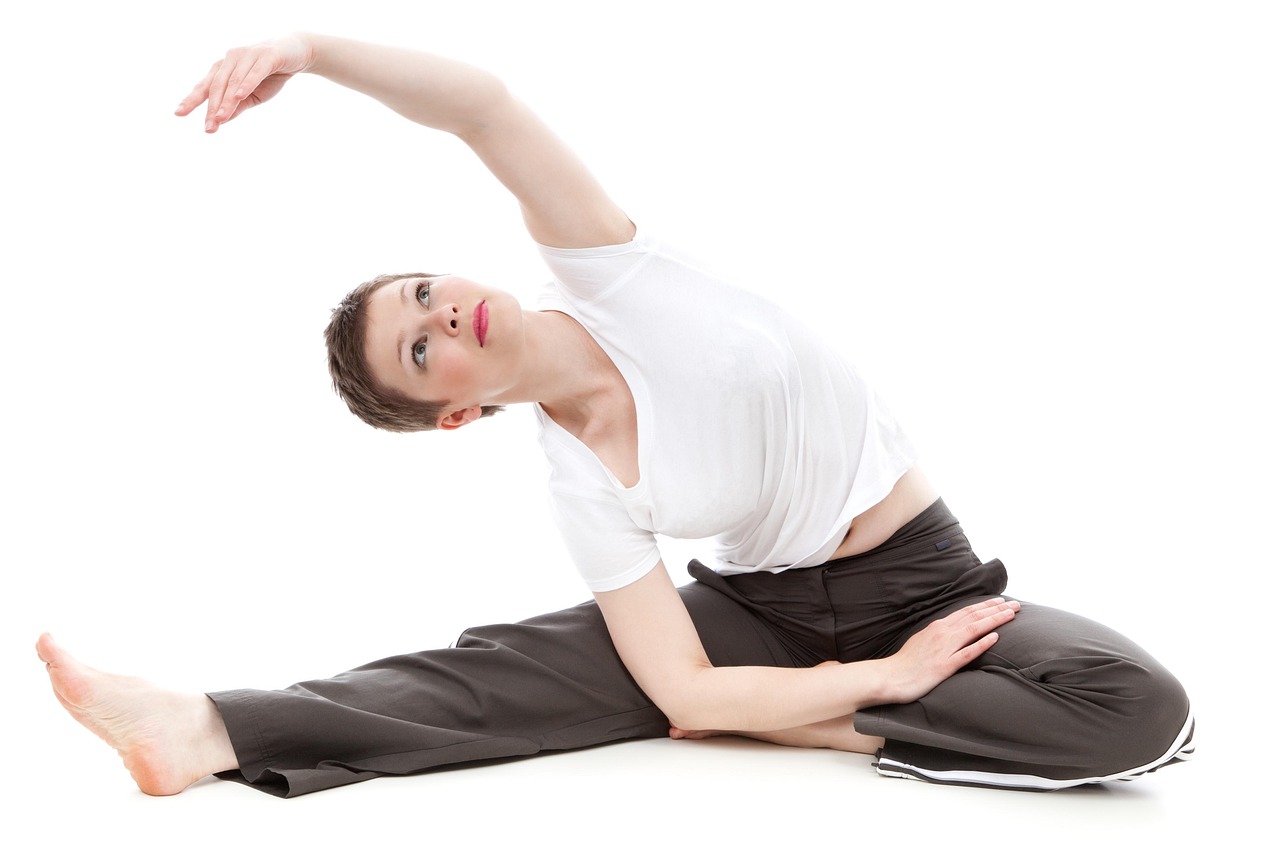 A young woman in a yoga pose. She is wearing a white t-shirt and black pants. Her body is in a side lunge position with her l...