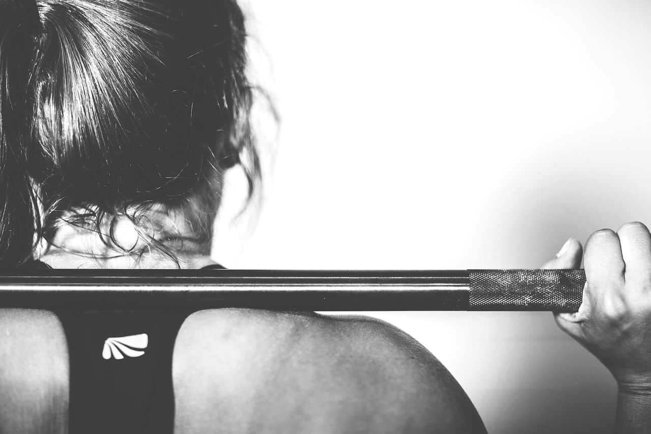 A black and white photograph of a person lifting a barbell. The person is holding the barbell with both hands and their face ...