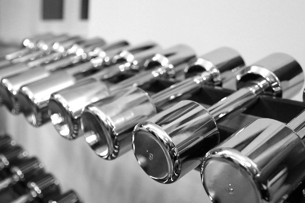 A black and white photograph of a row of dumbbells. The dumbbell weights are arranged in a neat and orderly manner, with each...