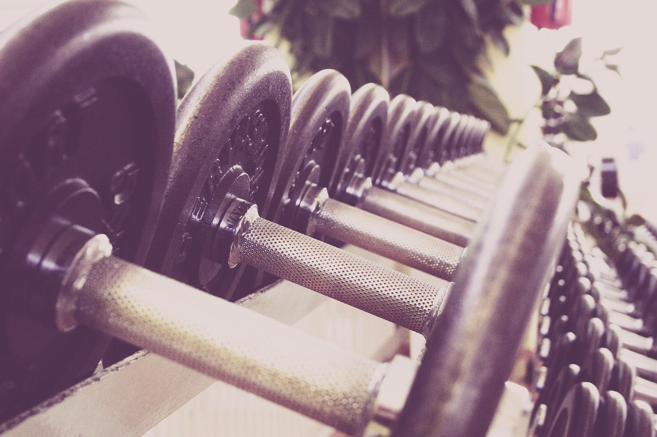 A row of dumbbells in a gym. The dumbbell on the left side of the image is black and appears to be made of metal, while the o...