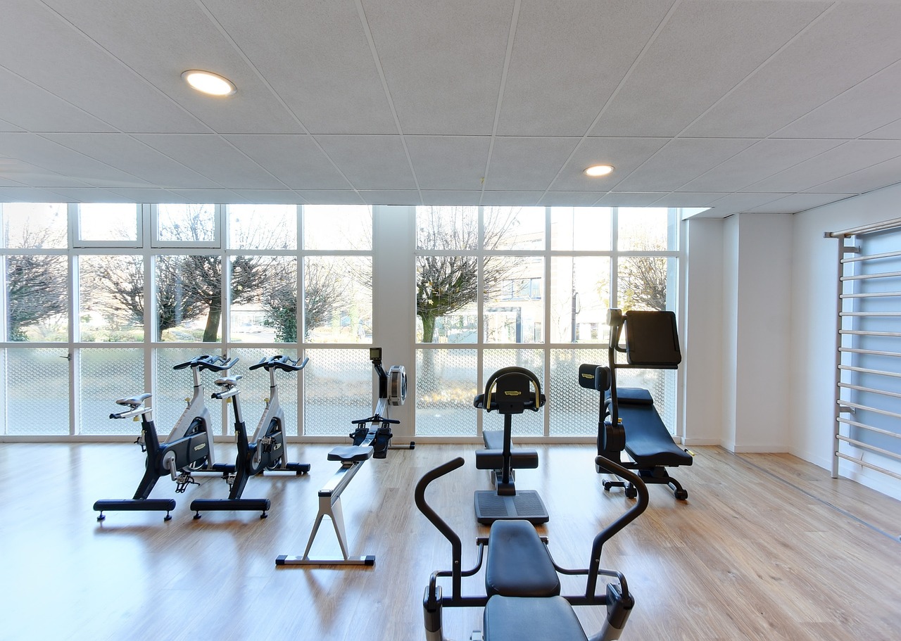 An empty gym with a large window that offers a view of the outside. The floor is made of light-colored wood and the walls are...