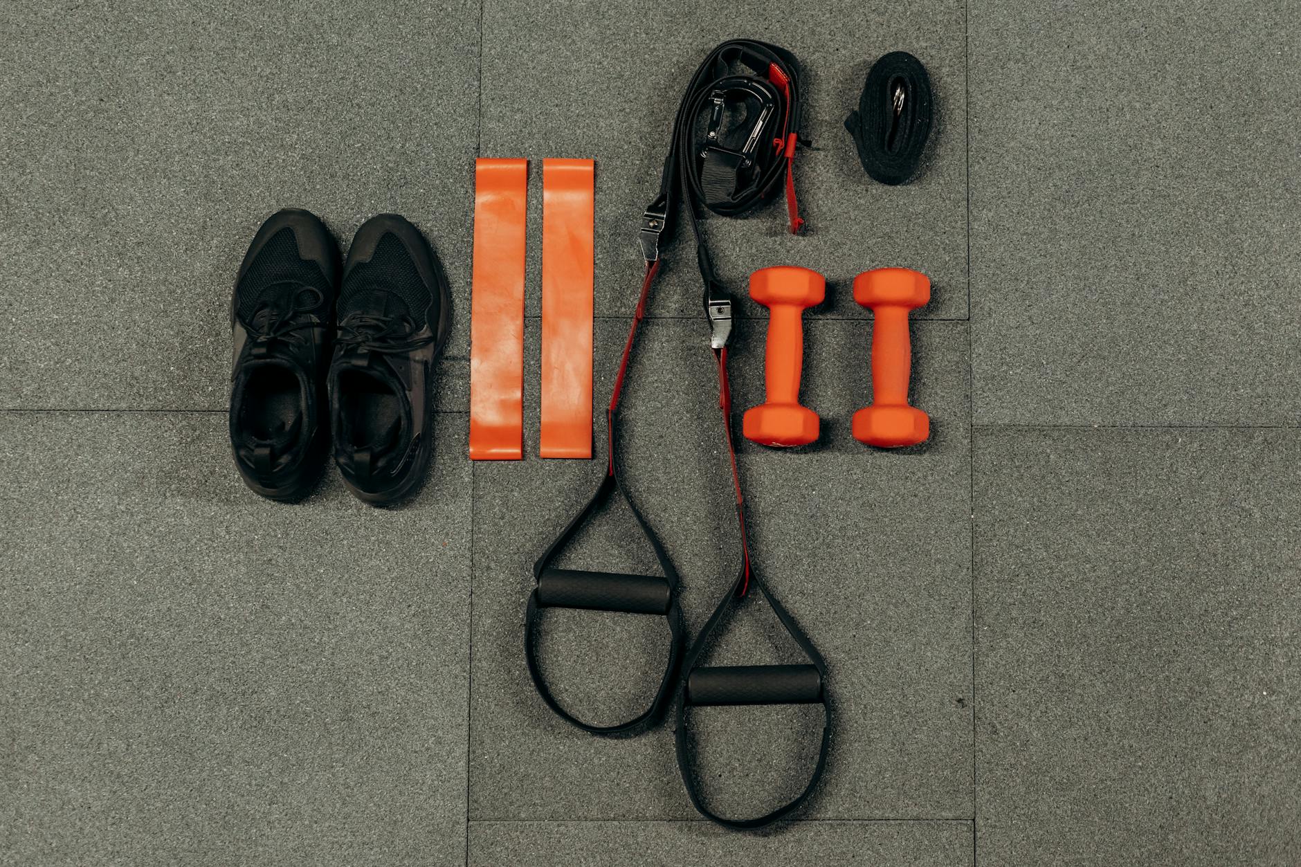 A set of fitness equipment laid out on a gray tiled floor. On the left side of the image, there is a pair of black sneakers, ...
