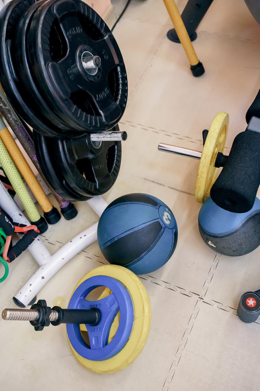 A gym floor with various exercise equipment scattered on it. On the left side of the image, there is a black barbell with a w...