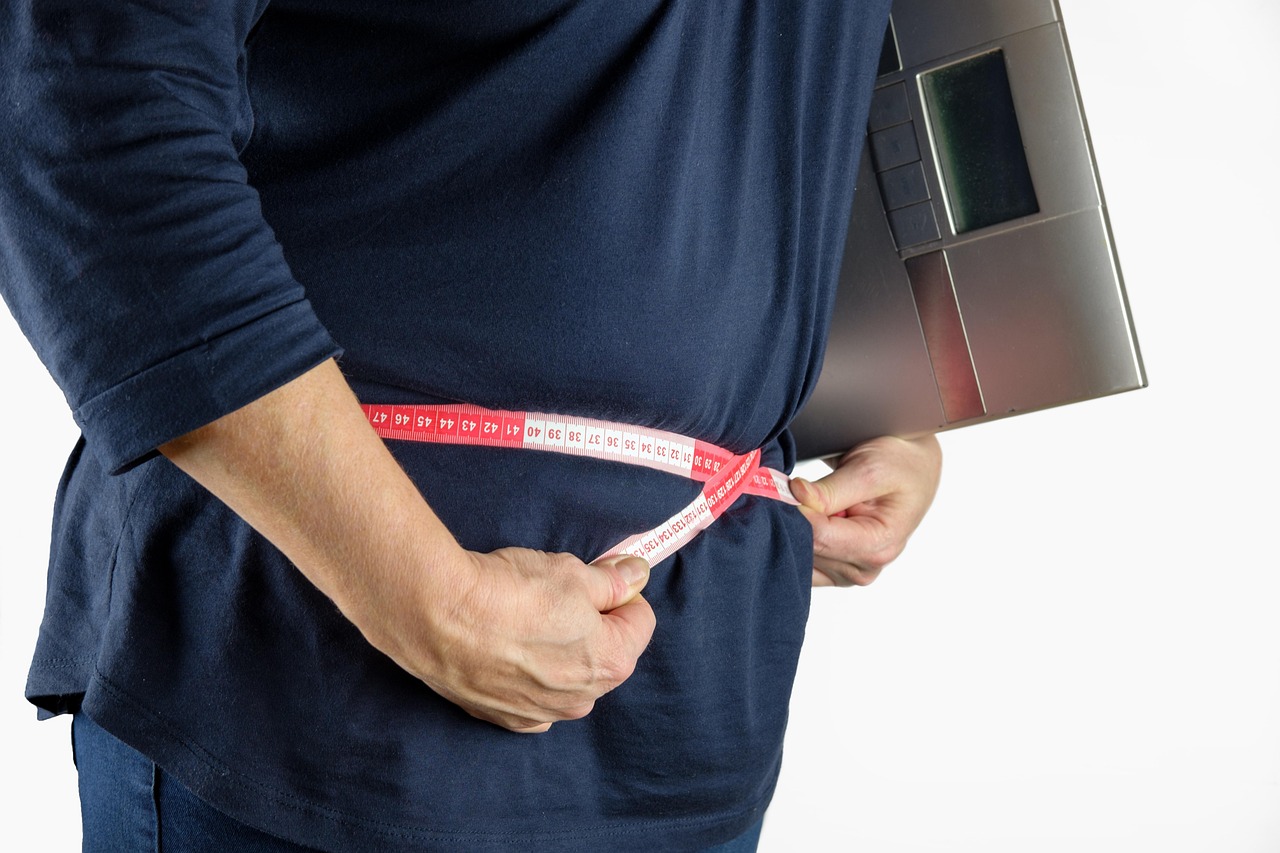 A person standing in front of a weighing scale. The person is wearing a dark blue t-shirt and is holding the scale with both ...