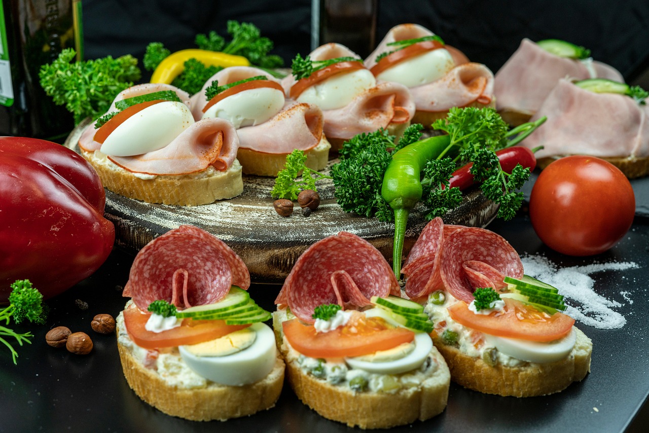 A platter of appetizers on a black plate. The platter is made of wood and is decorated with various types of food. On the lef...