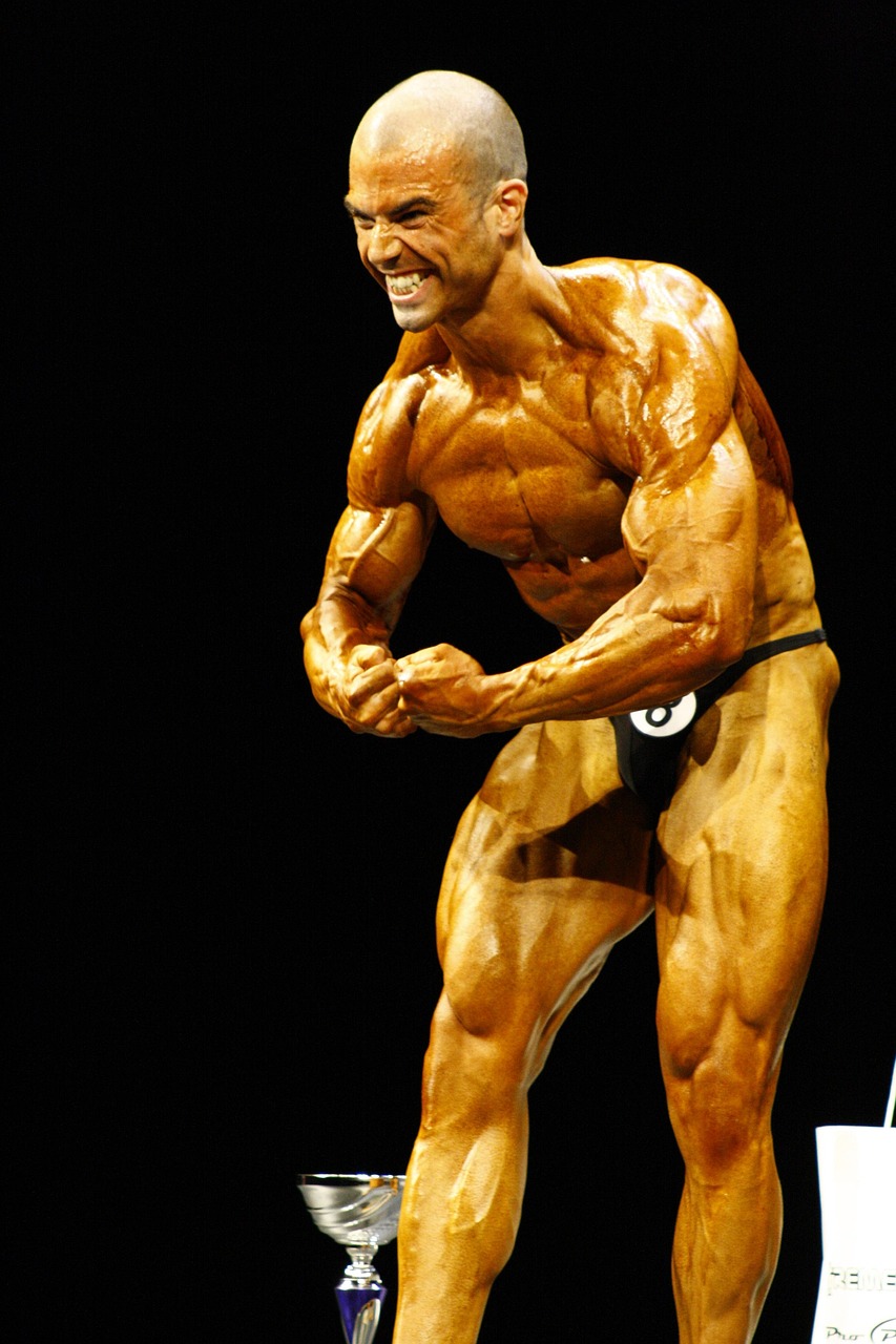 A bodybuilder standing on a stage with a trophy in front of him. He is wearing a black thong and is flexing his muscles, show...