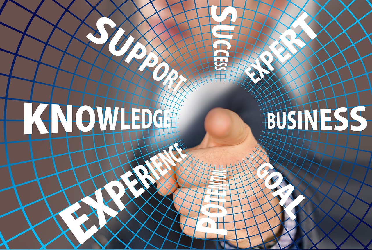 A hand pointing towards a blue grid-like background with the words "knowledge", "experience", "success", "expert", "business"...