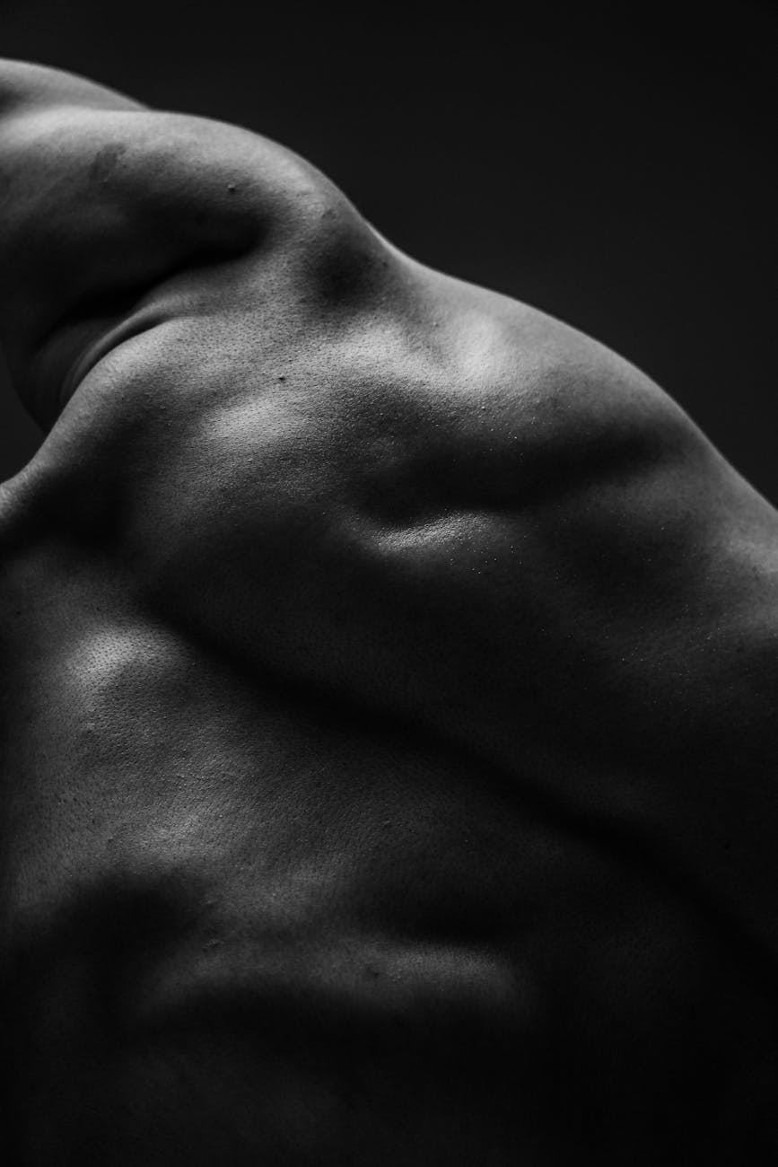 A black and white close-up of a person's torso and upper body. The person appears to be in a relaxed pose, with their arms st...